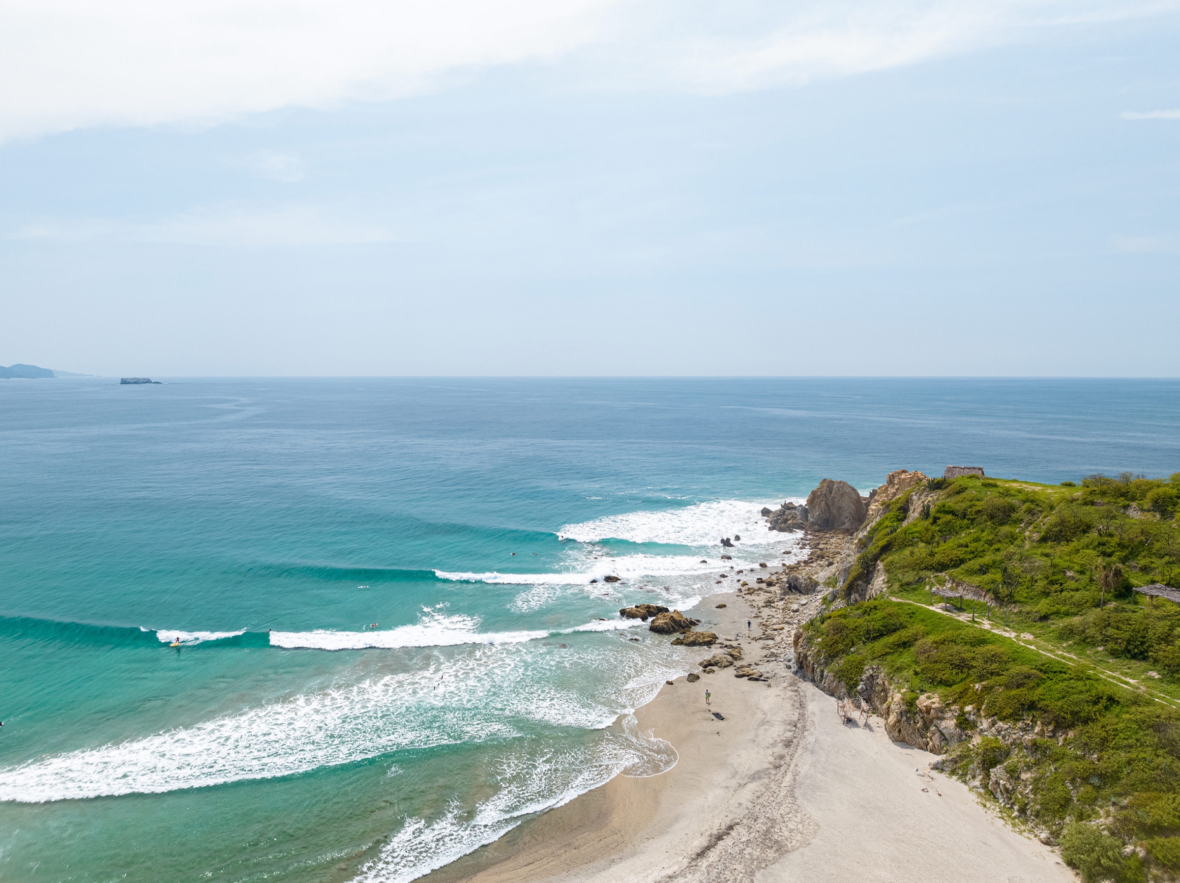 Aerial of a turquoise point break wrapping around a green headland