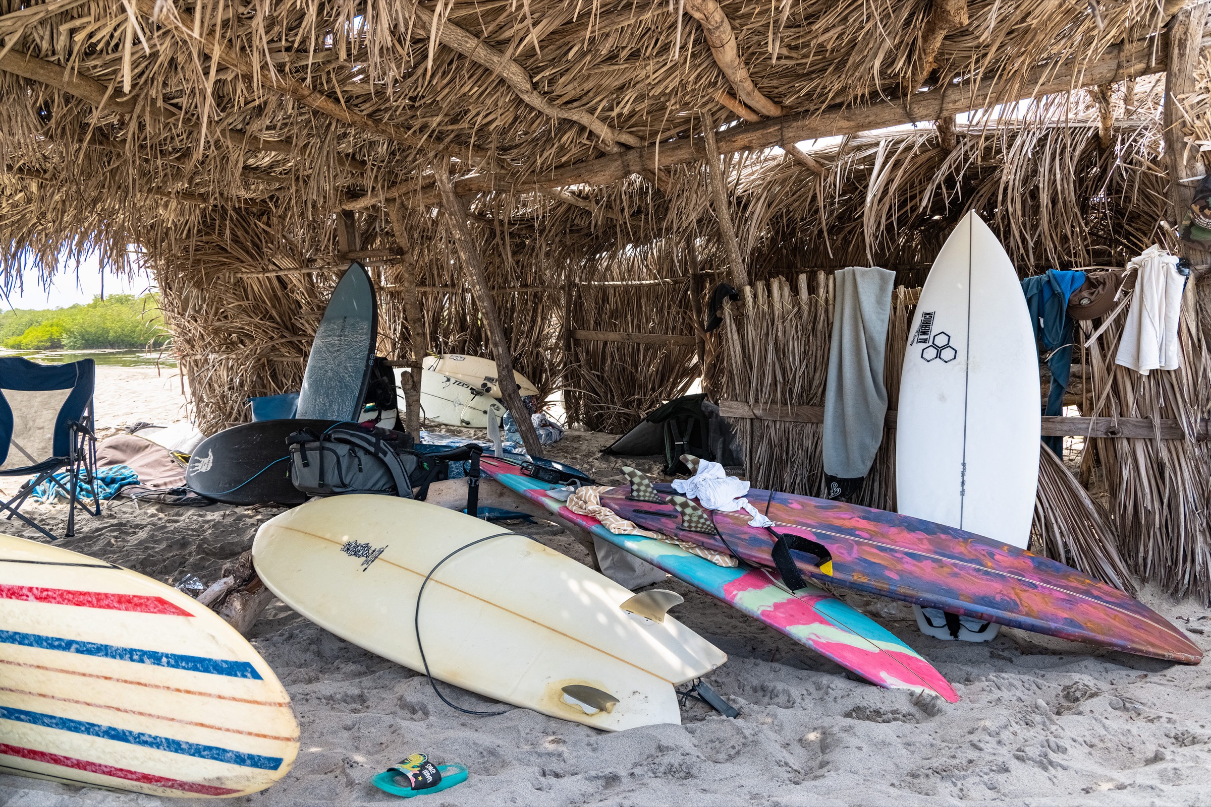 A quiver of surfboards leaning under a thatched palapa on the sand